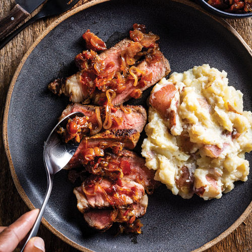 Ribeye steak with bacon-bourbon compote and mashed potatoes, an American Queen Voyages dish created with America's Test Kitchen.